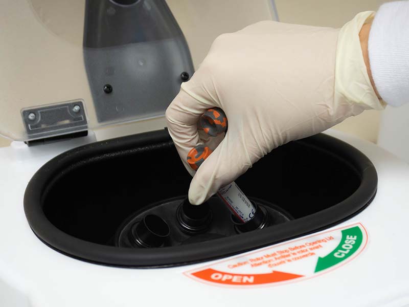 lab worker wearing gloves removes vials from centrafuge